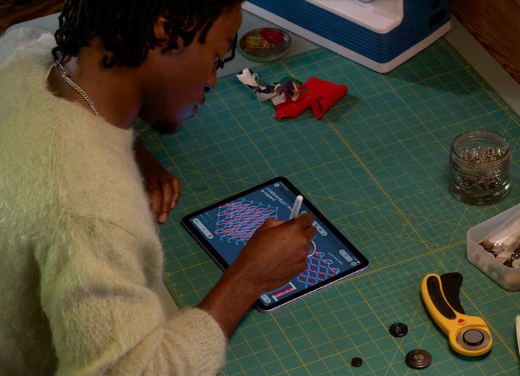 En person laver skitser med Apple Pencil på iPad, siddende ved et grønt skæreunderlag med sygrej.
